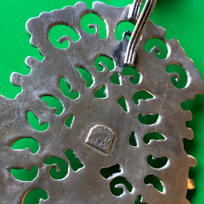 Closeup shot of the backside of the pendant on a green wood surface, showing the 925 stamp indicating the piece is sterling silver.