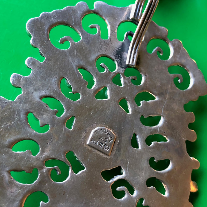 Closeup shot of the backside of the pendant on a green wood surface, showing the 925 stamp indicating the piece is sterling silver.