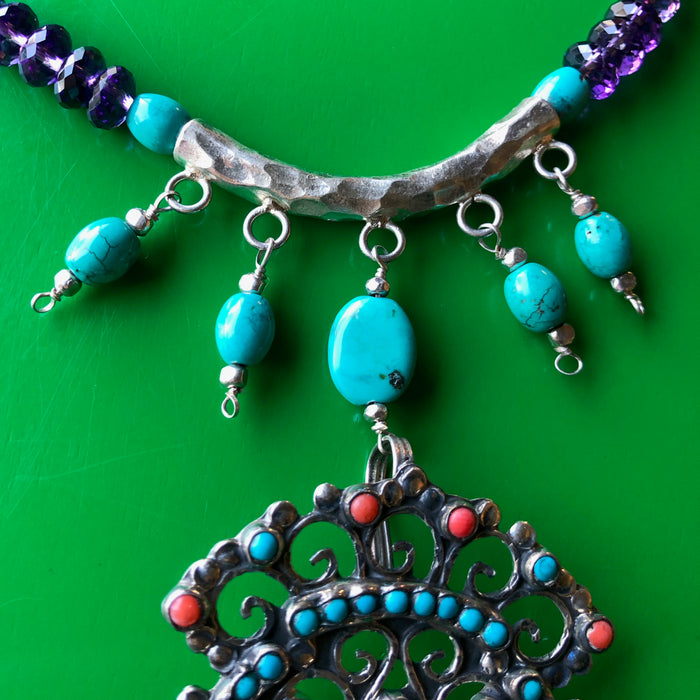 Close up shot of the fine turquoise beads hanging from the hand hammered Hill Tribe pure silver pendant. The image is cropped in close, showing off the piece in focus with lots of detail laying on a bright green wooden surface.