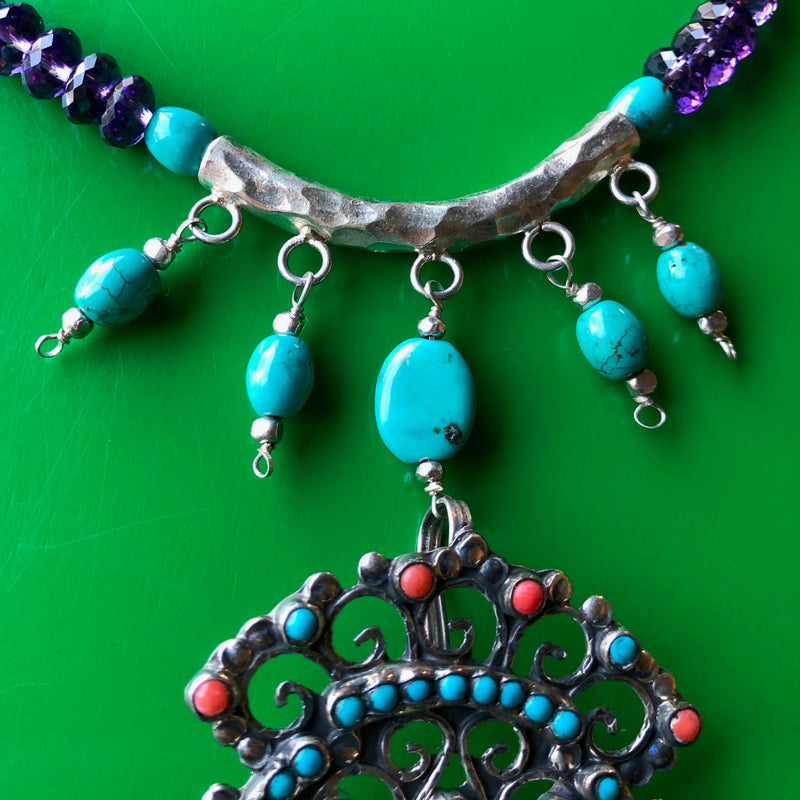 Close up shot of the fine turquoise beads hanging from the hand hammered Hill Tribe pure silver pendant. The image is cropped in close, showing off the piece in focus with lots of detail laying on a bright green wooden surface.