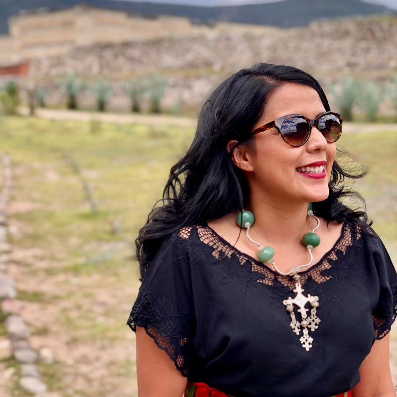 Smiling model with long black hair in Mitla archaeological site in Oaxaca, Mexico wearing sunglasses, a black crochet top, sunglasses and the handmade beaded necklace with vintage sterling silver Yalalag cross pendant, large faceted jade beads, small spring jade beads, large Hill Tribe pure silver spacers and nuggets, sterling silver toggle clasp.