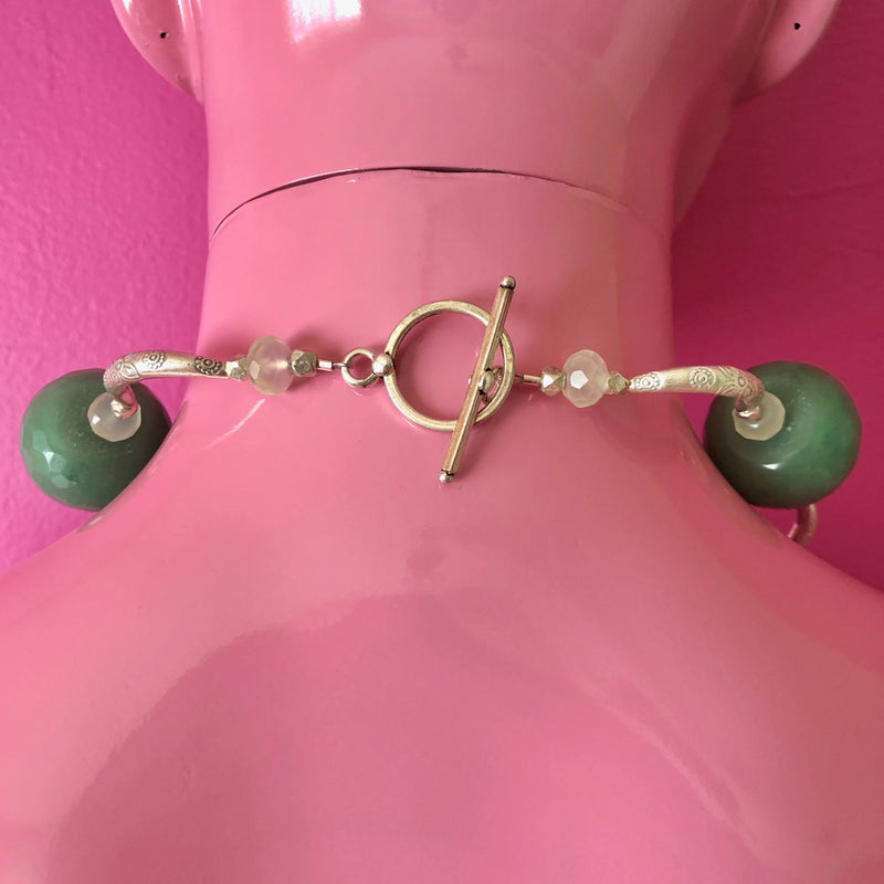 Close up of the toggle clasp and some of the handmade beaded necklace with vintage sterling silver Yalalag cross pendant, large faceted jade beads, small spring jade beads, large Hill Tribe pure silver spacers and nuggets. Shown on a pink mannequin facing a darker pink wall.