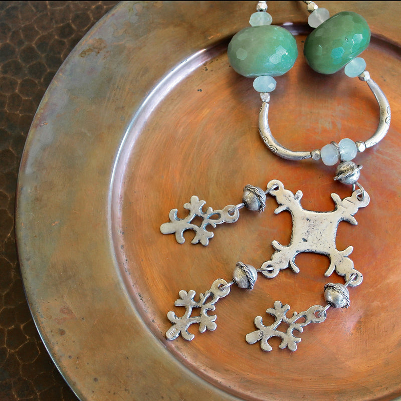 Close up, cropped, detailed overhead shot of the Yalalag pendant necklace with green jade beads, and Hill Tribe pure silver spacers laying on bright copper plate that sits on a dark brown, hand hammered copper surface. The image is cropped and the portion the necklace in focus. 