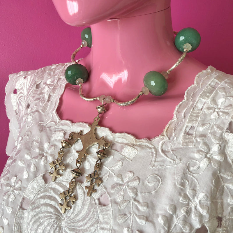 Pink mannequin at three quarter view in front of a darker pink wall wearing a white embroidered huipil from the Yucatan and the handmade beaded necklace with vintage sterling silver Yalalag cross pendant, large faceted jade beads, small spring jade beads, large Hill Tribe pure silver spacers and nuggets, sterling silver toggle clasp. The image is cropped from the chin to the top of the breast of the mannequin, showing off the necklace in focus with lots of detail.