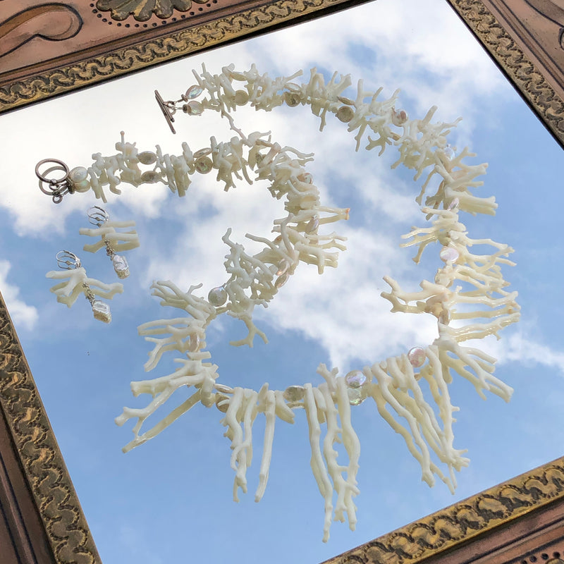An overhead shot of the White Branch Coral and Coin Pearls Necklace and Earring Set, with the entire set in focus including the toggle clasp in the background. Laying on a vintage Mexican metal framed mirror, the necklace appears to be floating in the cloudy blue sky.