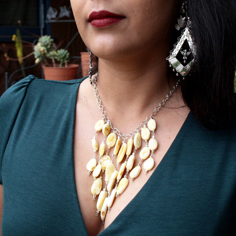 Close-up shot of Brenda modeling the Butterscotch Baltic Amber on Sterling Silver Chain Necklace while wearing a dark teal dress with a deep v-neck that allows the necklace to fall flatteringly on the decolletage.