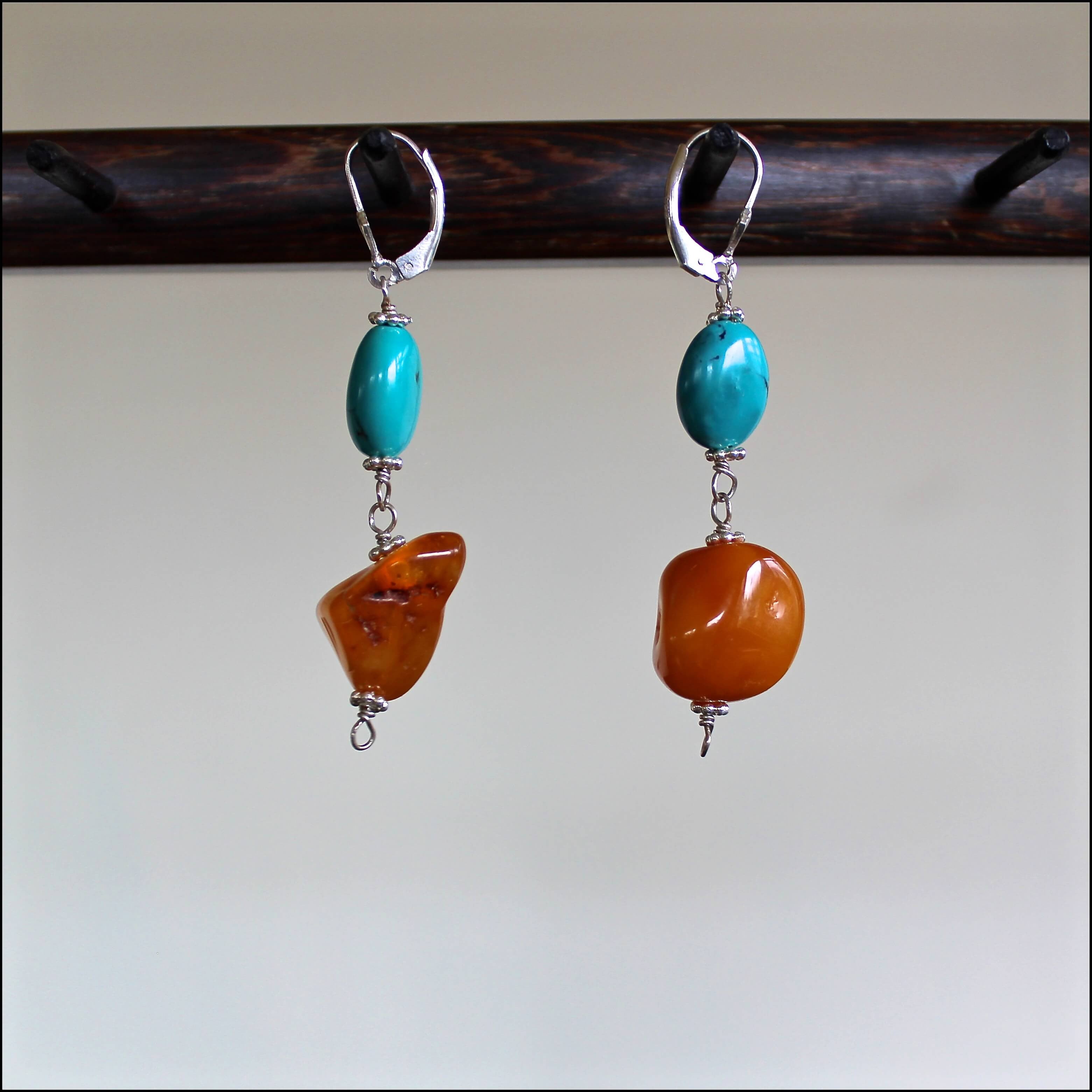 An eye level shot of the Butterscotch Baltic Amber Turquoise Bead and Sterling Silver Earrings hanging in front of a white background showing off the swirls inside of each opaque, one of a kind amber bead, and the minimal detail of the oval turquoise beads.