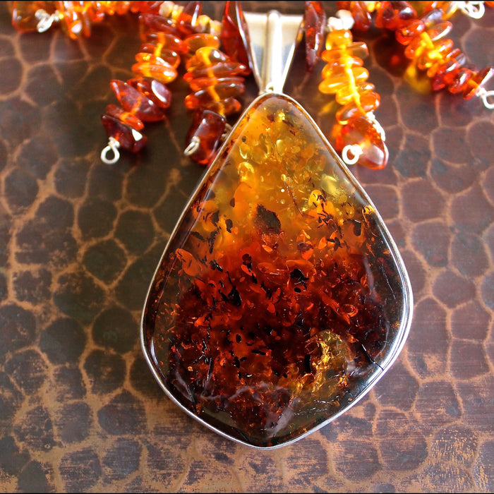 Close up shot of the whiskey Baltic amber pendant in sterling silver, showing the intricate texture and color gradient from dark reddish browns to golden yellows within the smooth, polished center piece of this statement necklace.